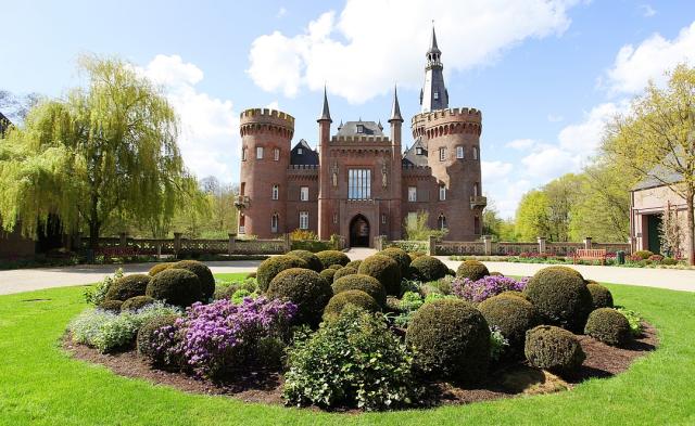 Fairytale castle Moyland in germany surrounded by manicured gardens and colorful flowers on a sunny day.