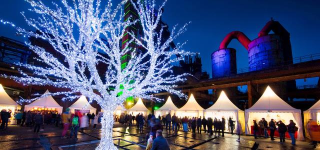 Weihnachtsmarkt bei Nacht mit beleuchtetem Baum und festlich geschmückten Ständen.